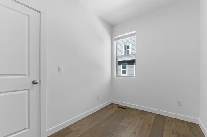 Wood-finish flooring with white baseboards, a single window with blinds, and a paneled door with a silver-tone knob