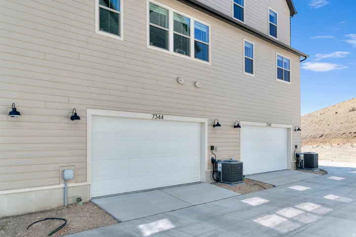 Tan horizontal siding exterior with multiple windows, two white garage doors, and exterior wall-mounted lighting fixtures
