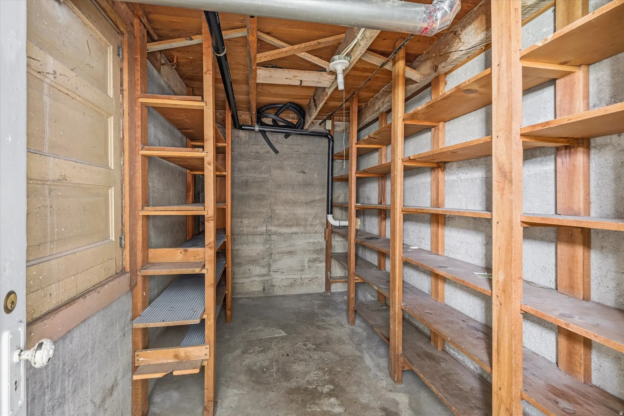 Basement storage area with extensive built-in wooden shelving, exposed concrete walls, and concrete flooring