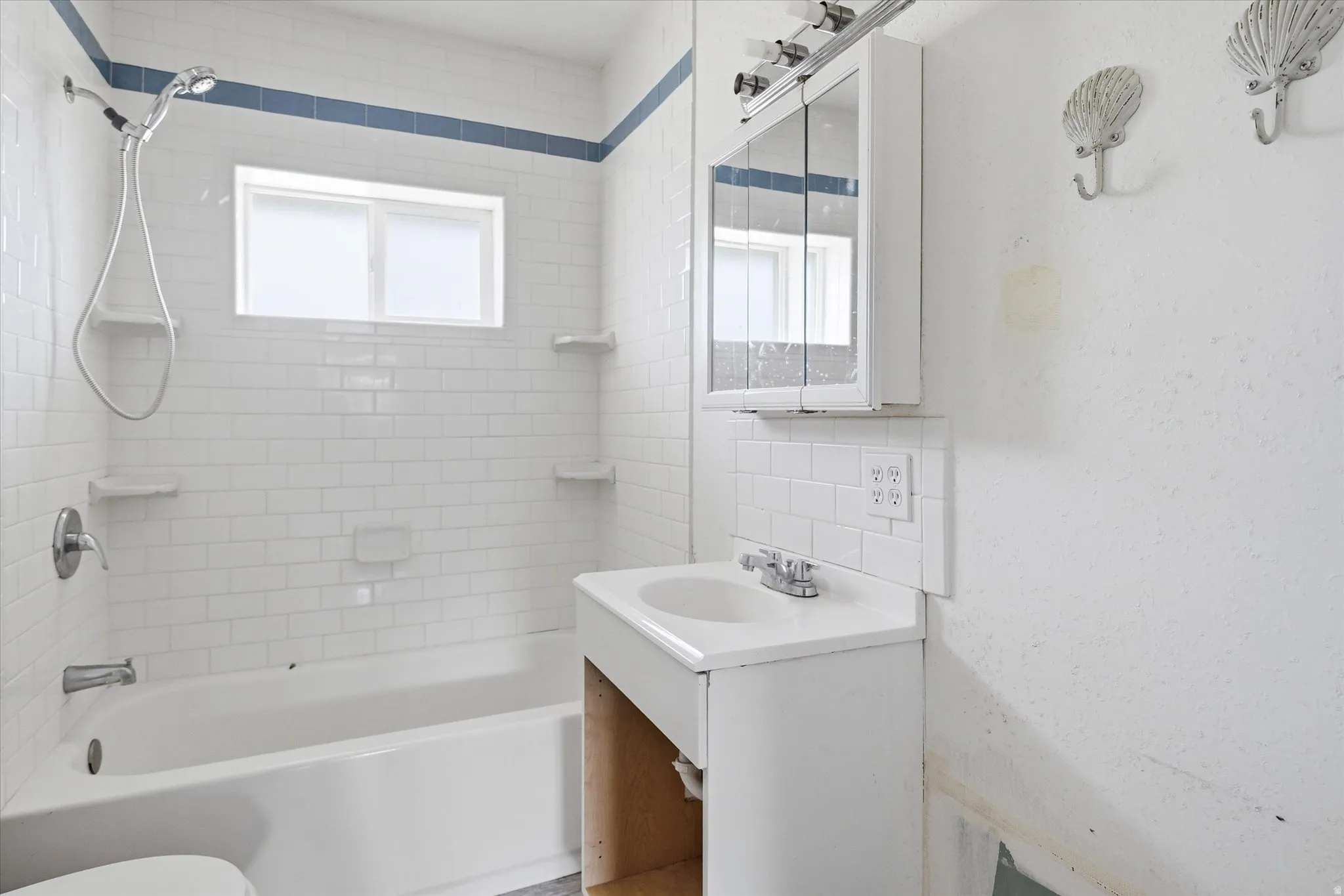 Bathroom featuring a white subway tile surround with a blue accent border, a white bathtub, and a window