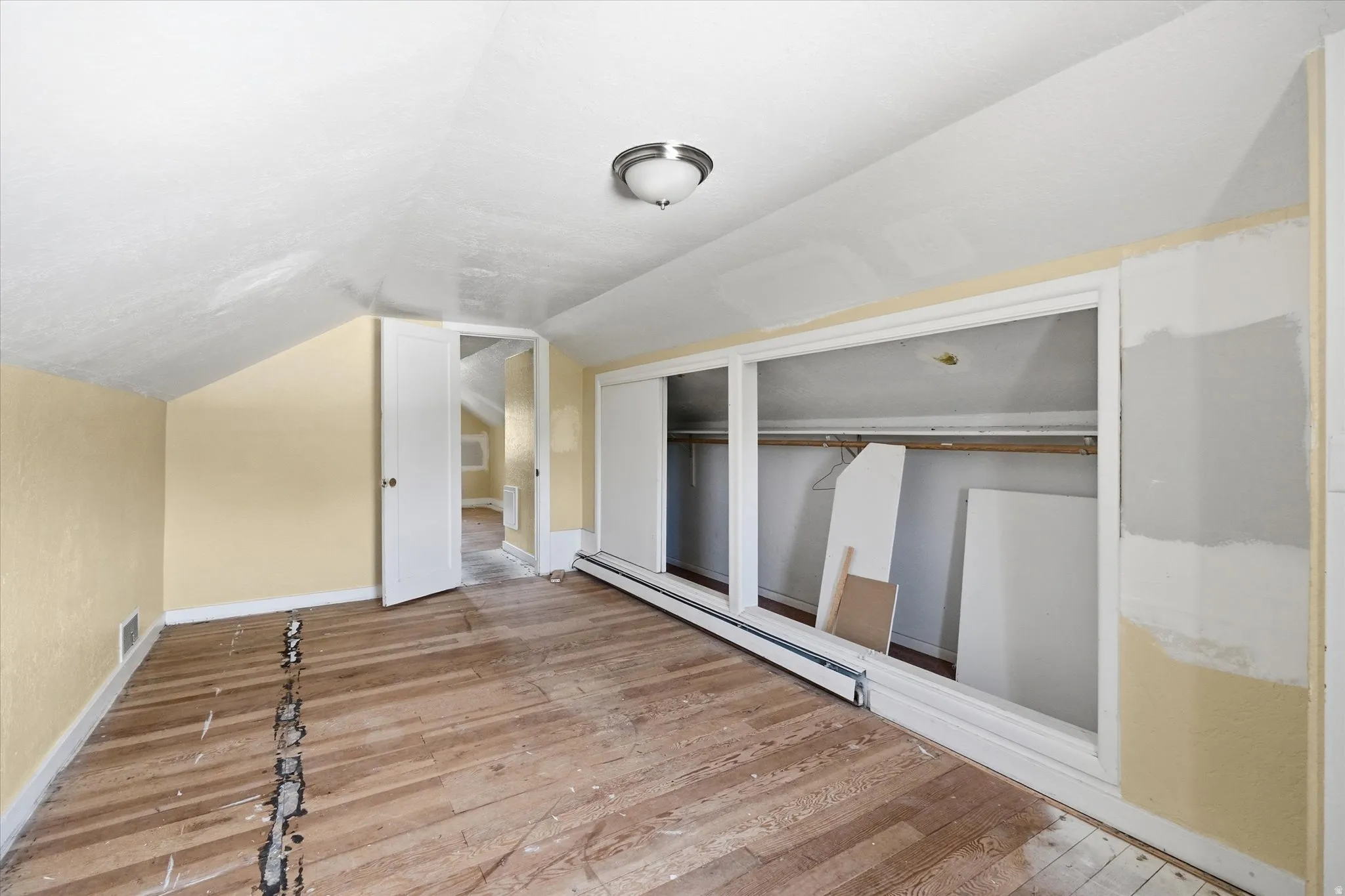 Room featuring a sloped ceiling, wood-finish flooring, and built-in closet space with sliding doors