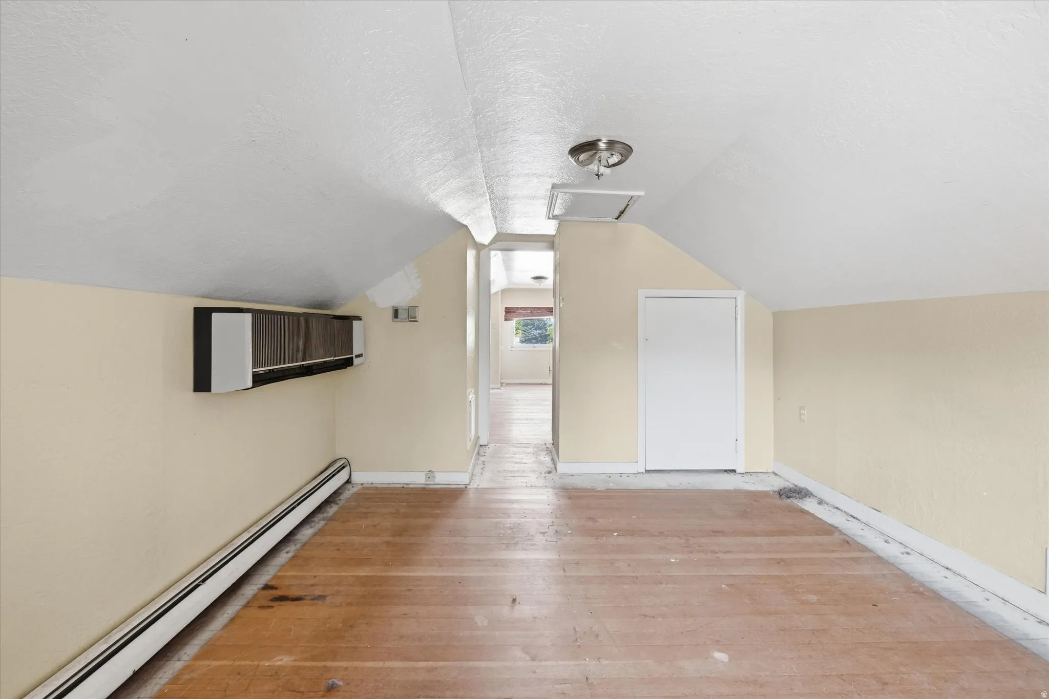 Attic space featuring wood-finish flooring, sloped white ceilings, and a light beige wall color