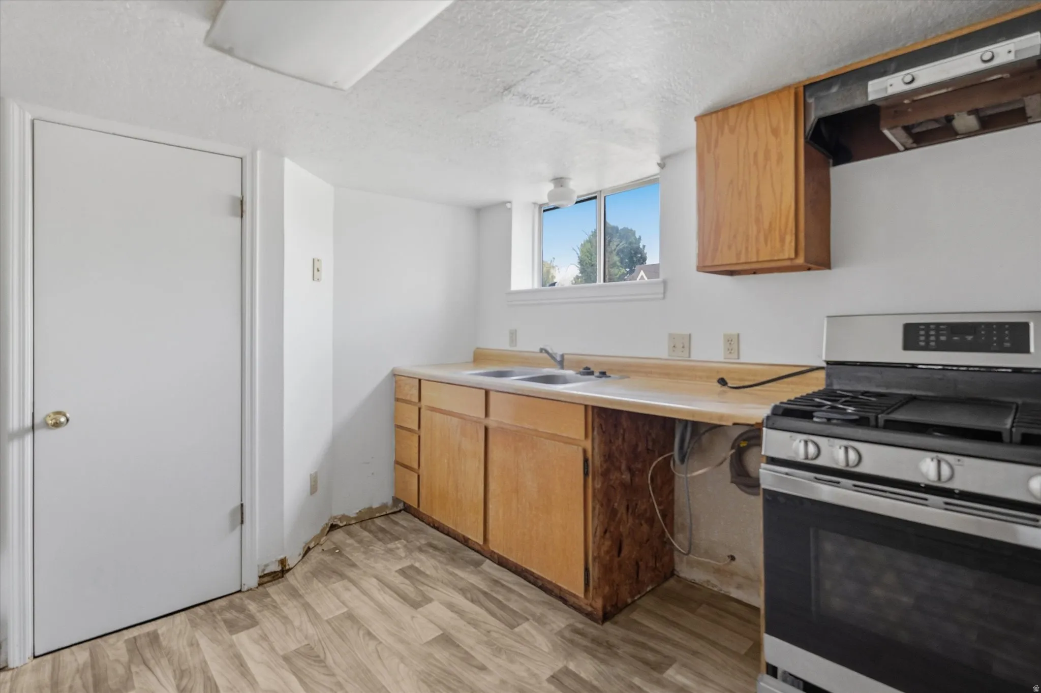 Kitchen area featuring wood-finish flooring, a stainless steel range, light wood cabinetry, and a double basin sink