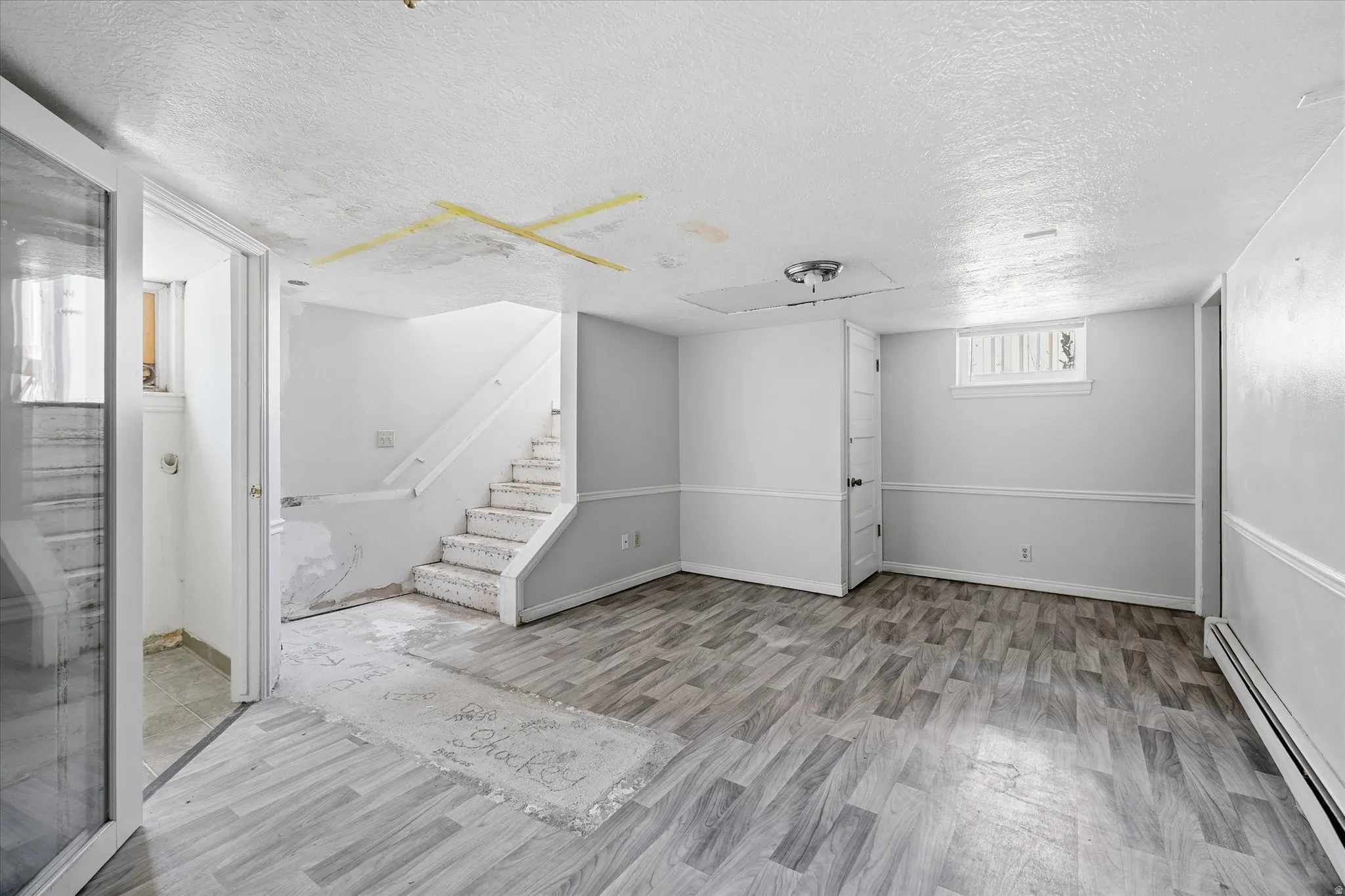 Spacious room featuring wood-finish flooring, light grey walls with white trim, and a window providing natural light