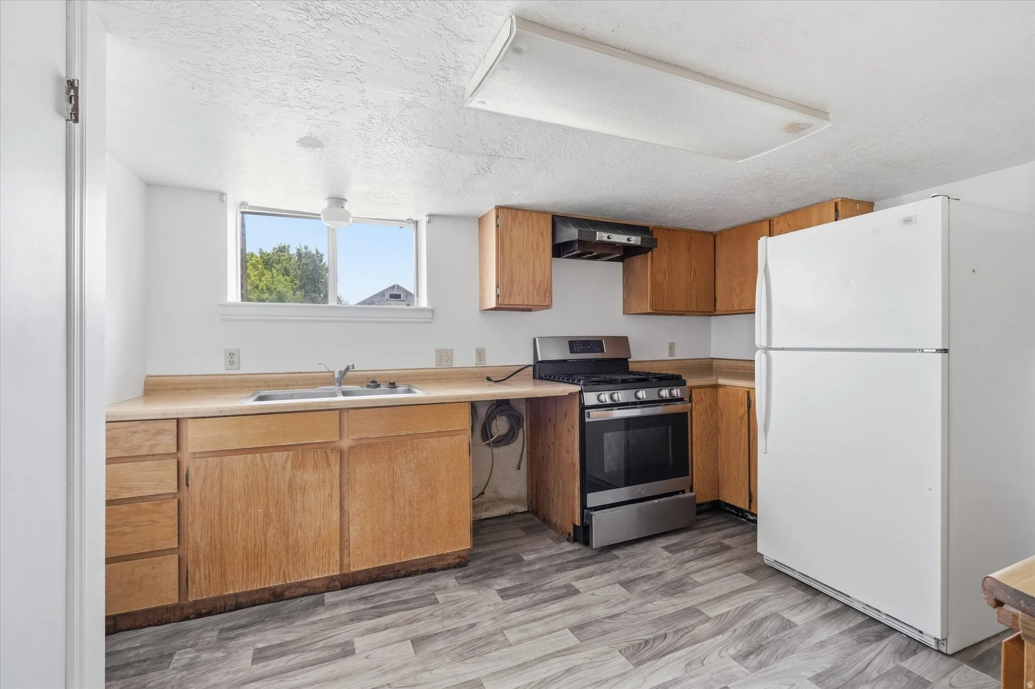 Kitchen featuring wood-finish flooring, light wood cabinetry, a stainless steel range, and a white refrigerator