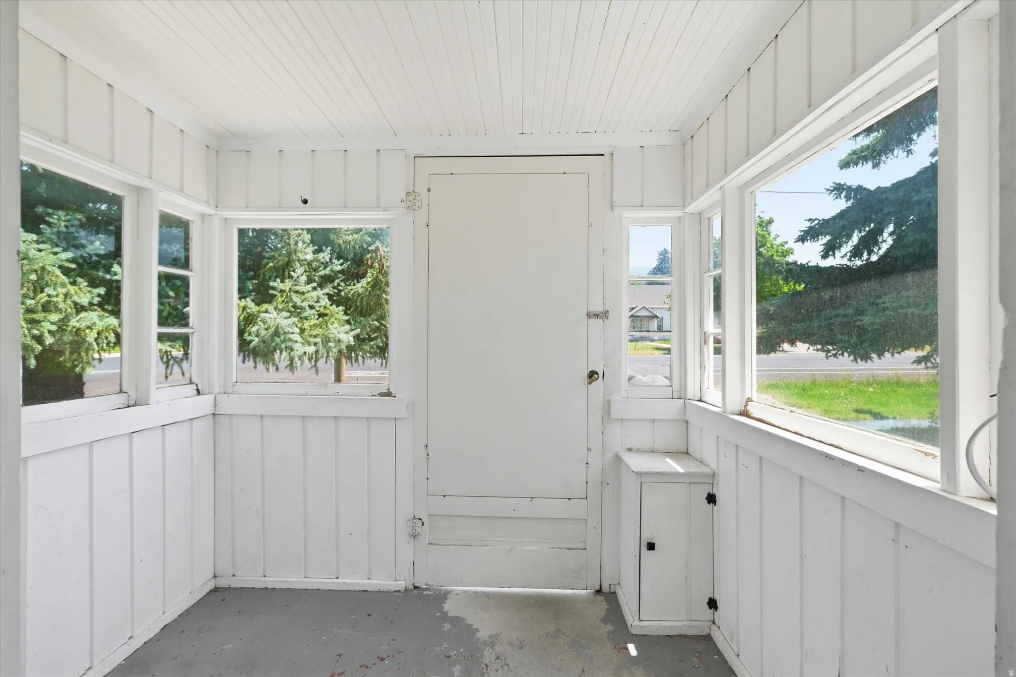 Enclosed porch with multiple windows, beadboard ceiling, white paneled walls, and built-in storage cabinet
