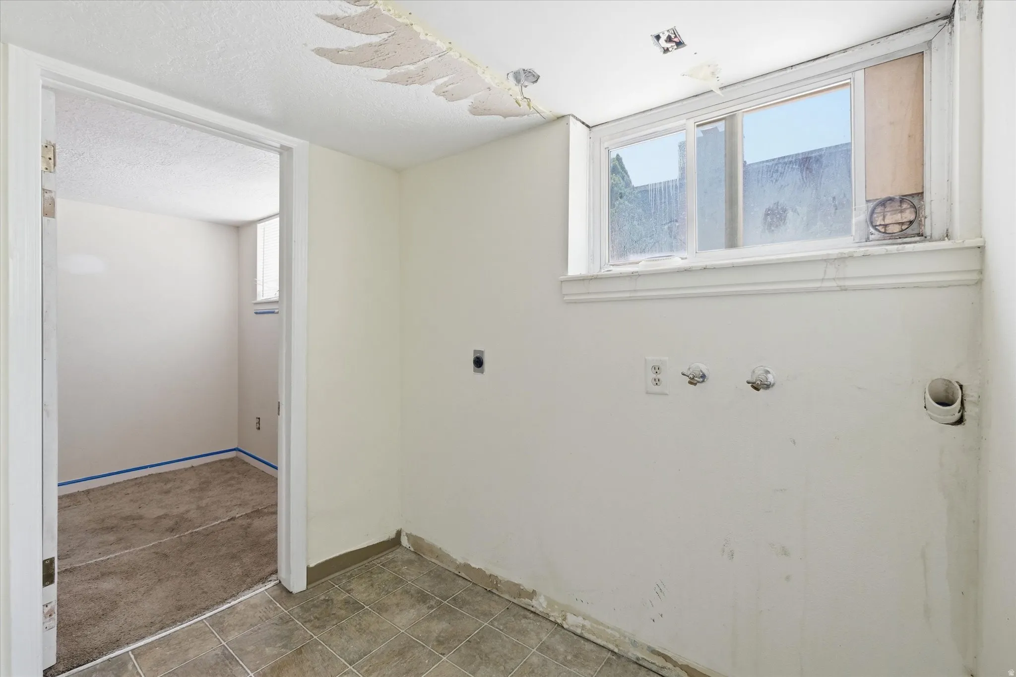 Utility space with tile flooring, a window, and exposed plumbing connections