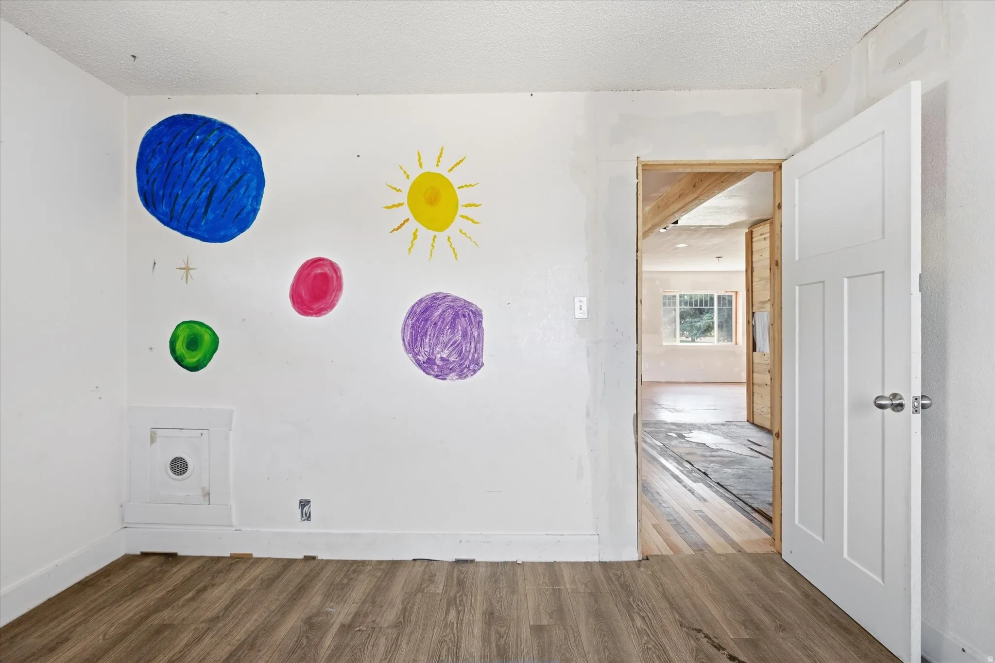 Interior space featuring wood-finish flooring, white baseboards, and a white paneled door with a chrome knob