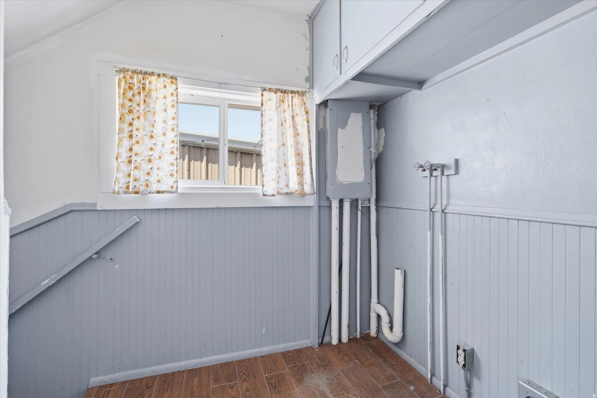 Utility space featuring a window, wood-finish flooring, beadboard wall paneling, and built-in cabinetry