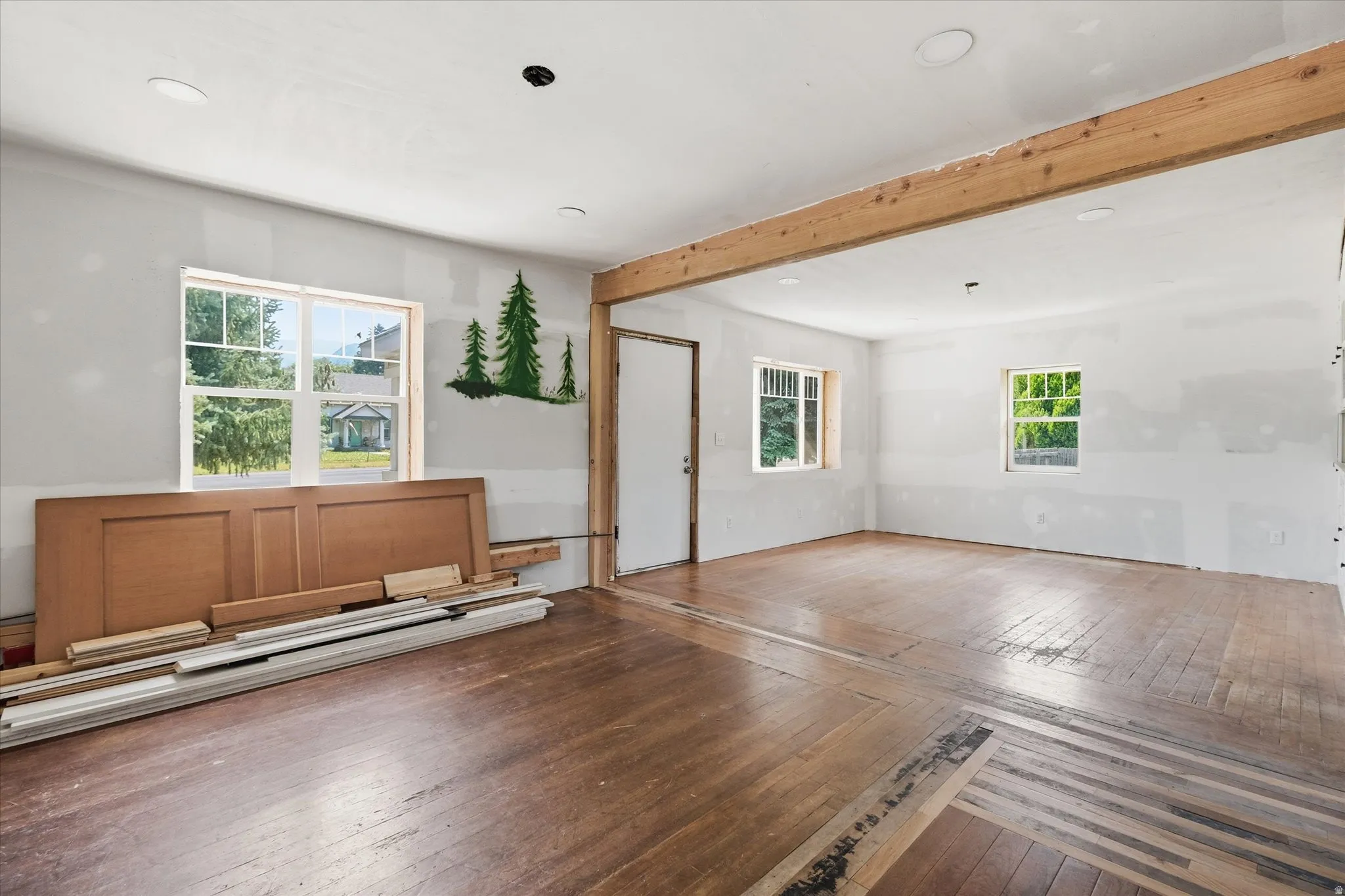 Expansive room featuring wood-finish flooring, exposed wood beam, multiple windows, and recessed lighting