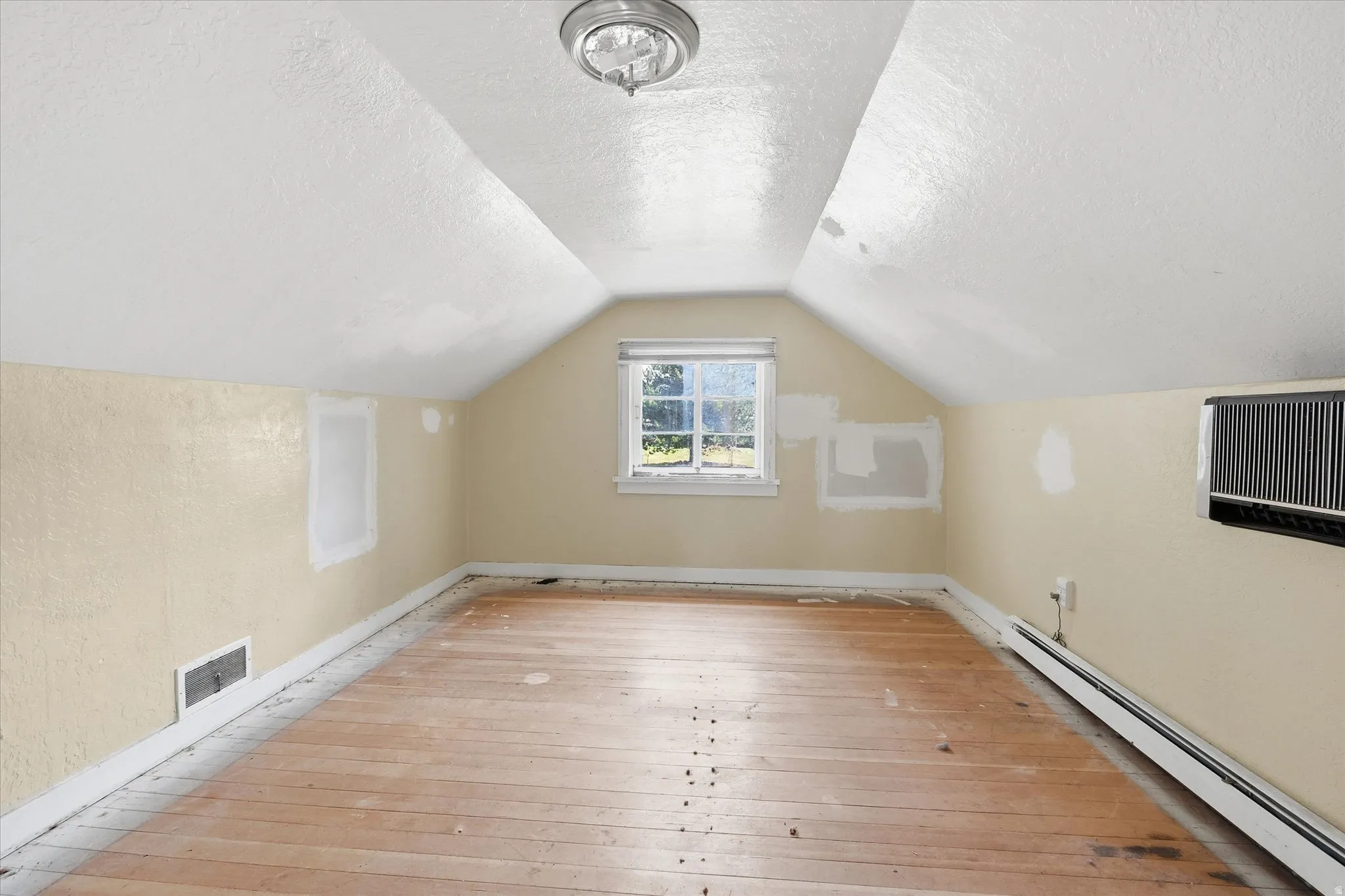 Spacious room featuring sloped ceilings, a window, wood flooring, and a ceiling-mounted light fixture