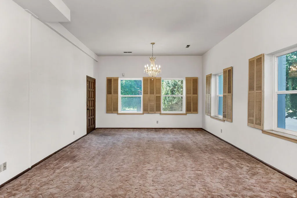 Spacious interior room featuring multiple windows with louvered shutters, a paneled door, and a chandelier