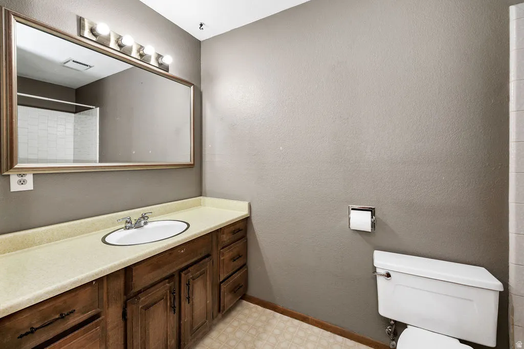 Bathroom featuring a wood-finish vanity with an oval sink, an expansive framed mirror, and a wall-mounted light fixture