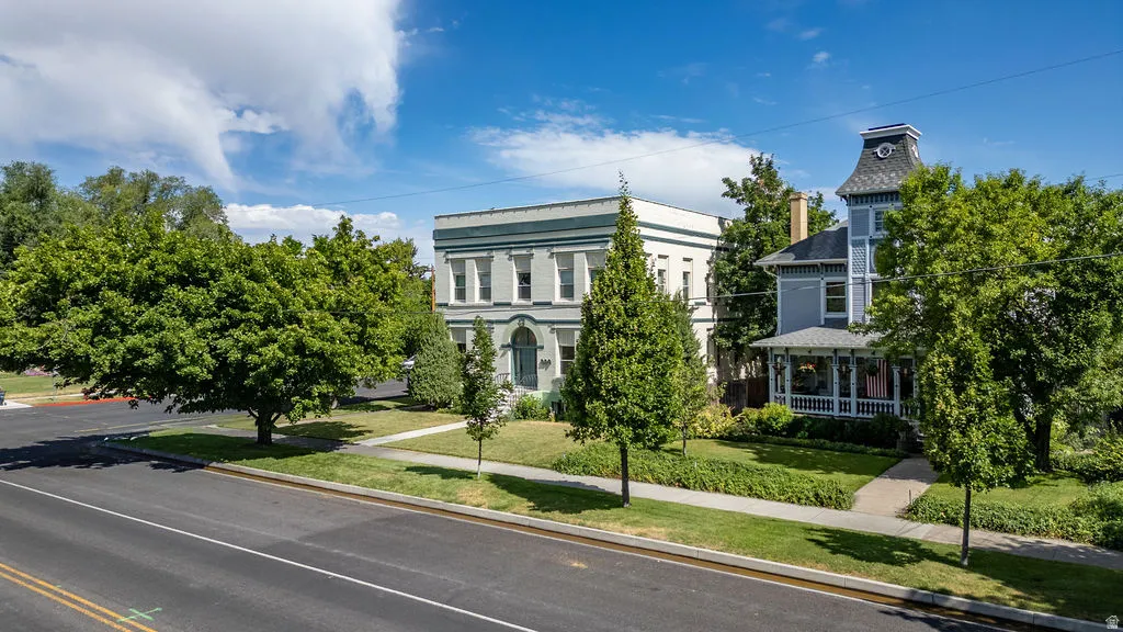 Historic-style residence featuring a prominent turret, covered porch with white railing, and a mature tree-lined street frontage
