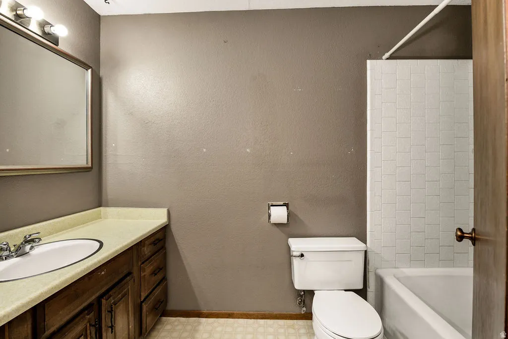 Bathroom featuring a wood-finish vanity with an integrated sink, a large wall-mounted mirror, a tiled shower-tub combination, and patterned floor tiling
