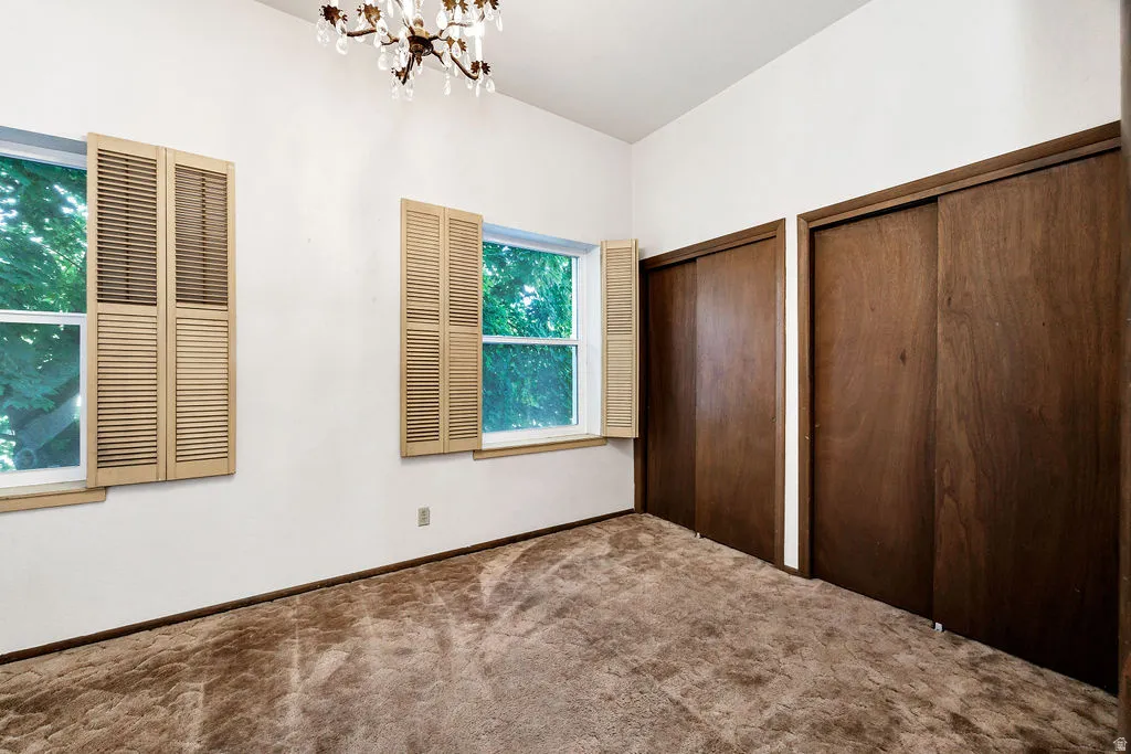 Bright room featuring two windows with louvered shutters, a crystal chandelier, and two spacious sliding-door closets with wood-finish doors