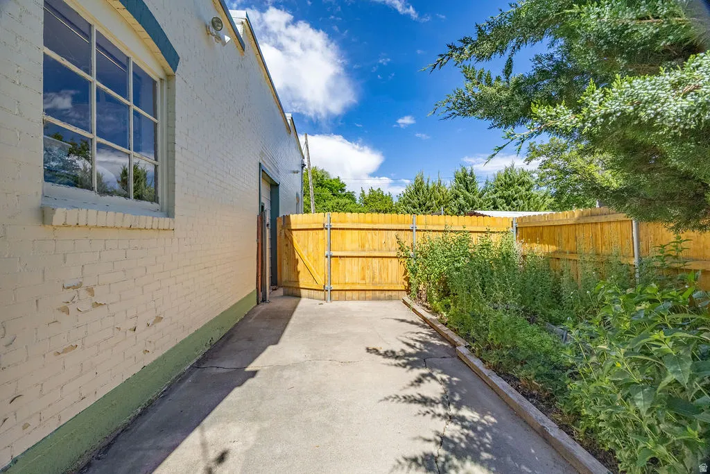 Paved exterior pathway featuring a vibrant wooden fence, a brick building with a large window, a side access door, and established greenery