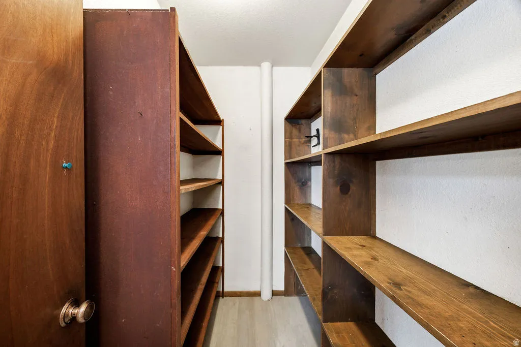 Dedicated storage room featuring extensive built-in wooden shelving, a solid wood-paneled door with a brass knob, light wood-finish flooring, and crisp white walls
