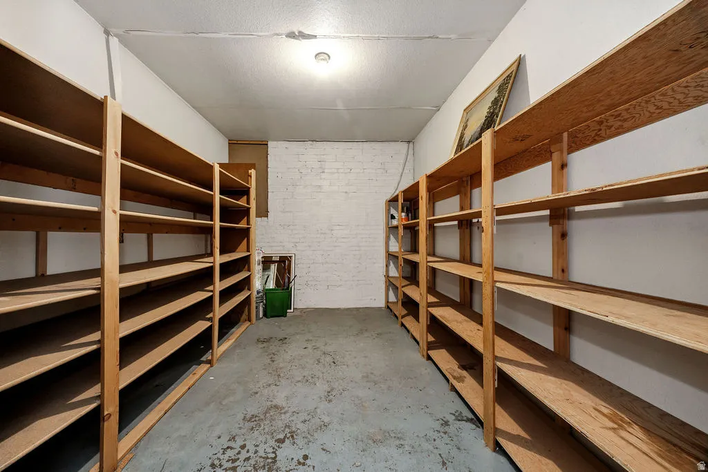 Dedicated storage room featuring extensive wood shelving, a painted concrete floor, and painted white brick wall