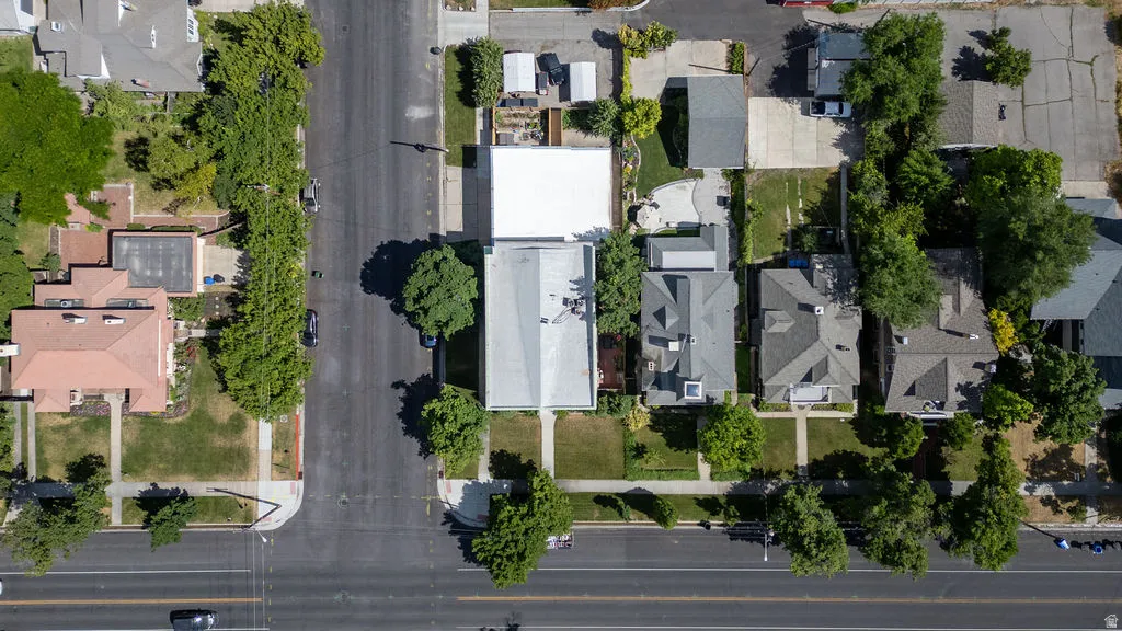 Aerial perspective showcasing a residential property with a light-colored roof, surrounded by mature trees and paved surfaces