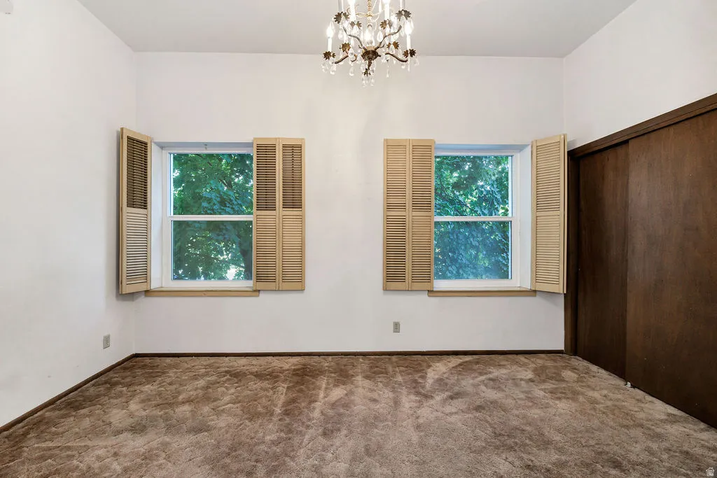 Room featuring two windows with louvered shutters, a built-in closet with dark wood sliding doors, and a decorative chandelier