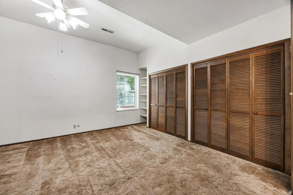 Spacious interior featuring two sets of louvered bi-fold closet doors, built-in shelving, a window providing natural light, and a ceiling fan