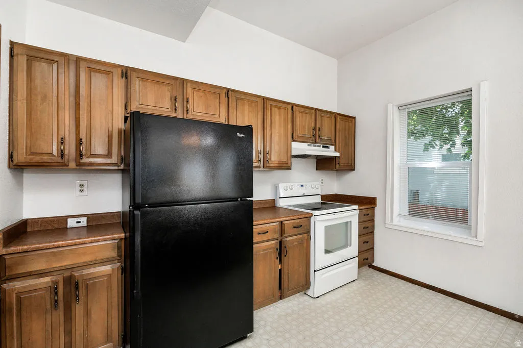 Kitchen featuring ample wood cabinetry, laminate countertops, a built-in range hood, an electric range, and a window