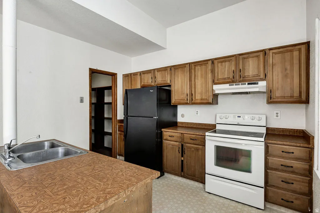 Kitchen featuring a double basin stainless steel sink, wood-finish countertops, black refrigerator, white electric range, and wood cabinetry with dark hardware