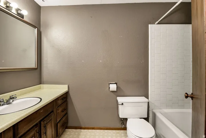 Bathroom featuring a wood-finish vanity with an integrated sink, a large wall-mounted mirror, a tiled shower-tub combination, and patterned floor tiling