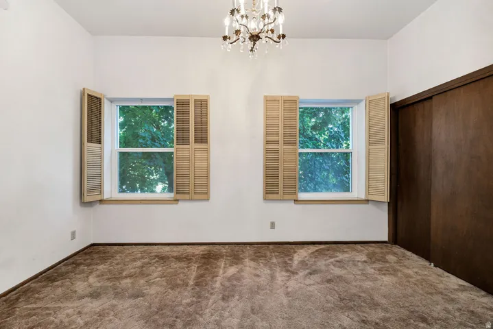 Room featuring two windows with louvered shutters, a built-in closet with dark wood sliding doors, and a decorative chandelier