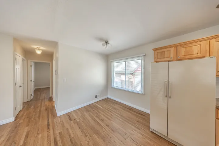 Kitchen area featuring wood-finish flooring, light-toned walls, a window with blinds, natural wood cabinetry, and a side-by-side refrigerator