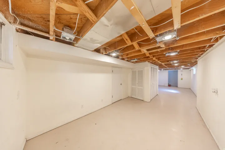 Expansive unfinished basement featuring exposed ceiling joists, recessed lighting, painted concrete flooring, and white painted walls