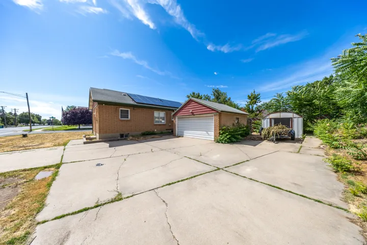 Expansive concrete driveway servicing a brick exterior residence, a detached garage with a red siding accent, and a separate storage structure