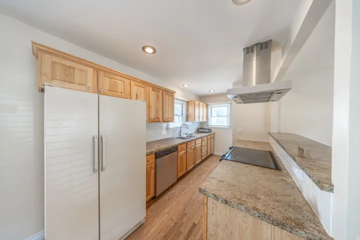 Kitchen featuring wood cabinetry, a stainless steel range hood, stone countertops, and wood-finish flooring