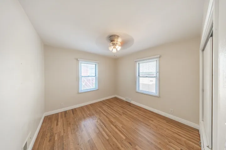 Spacious room featuring wood-finish flooring, light neutral wall tones, two windows with blinds, white trim, and a ceiling-mounted light fixture
