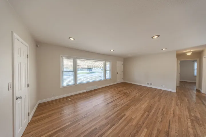 Spacious living area featuring wood-finish flooring, recessed lighting, and a large multi-pane window with blinds