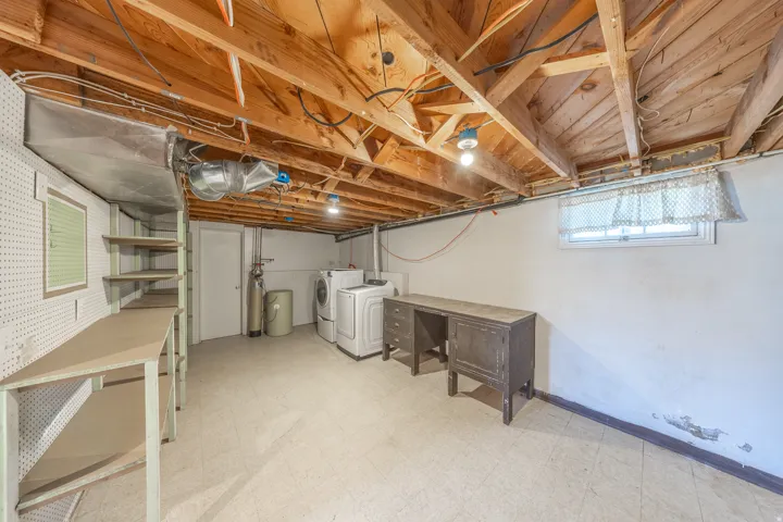 Spacious basement area featuring exposed wood joists, utility sink, washer and dryer, and built-in shelving