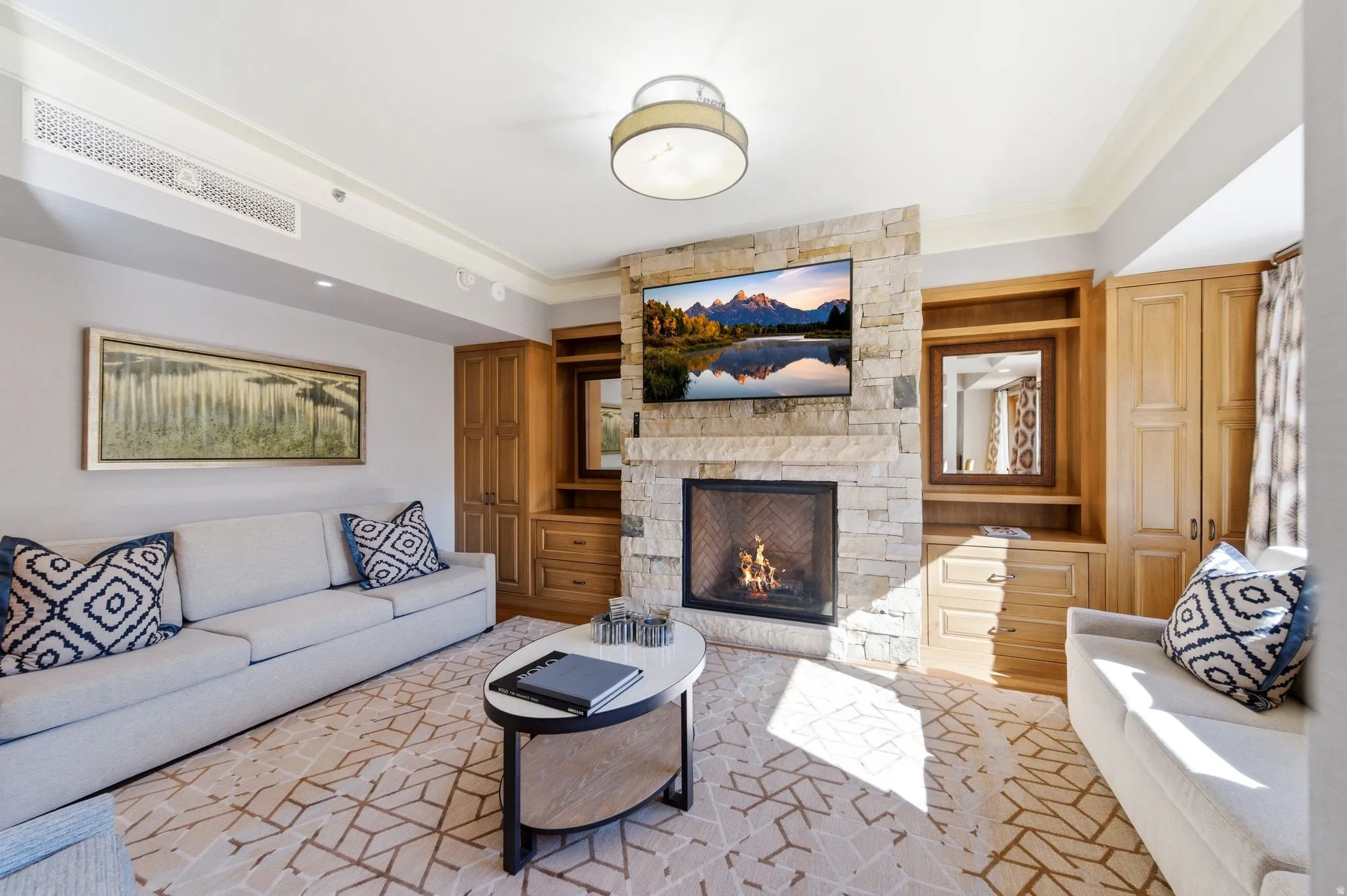 Stone fireplace feature wall with integrated television, custom built-in cabinetry, crown molding, and a patterned area rug
