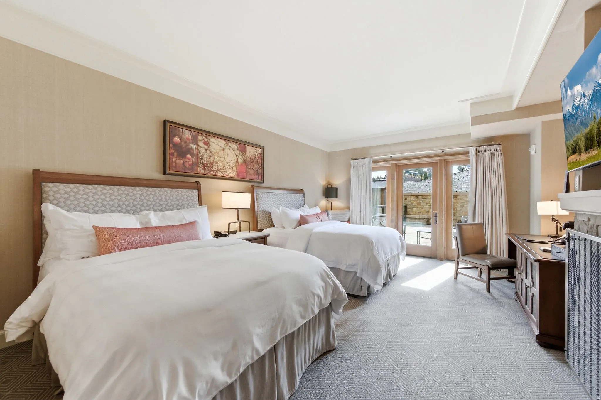 Bedroom featuring two beds with upholstered headboards, French doors opening to an exterior area, neutral-toned walls, and geometric pattern carpeting