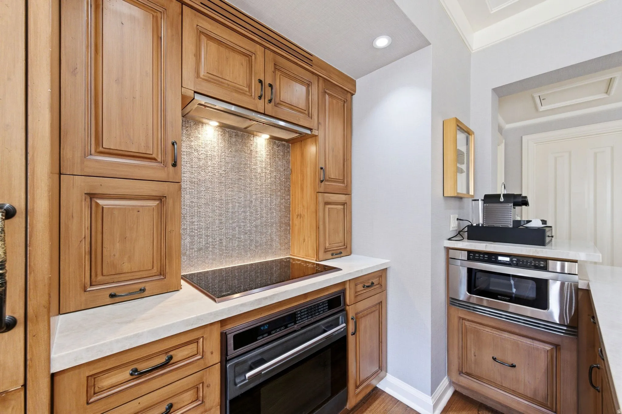 Built-in cooking station featuring a cooktop, integrated oven, under-cabinet lighting, and a tile backsplash