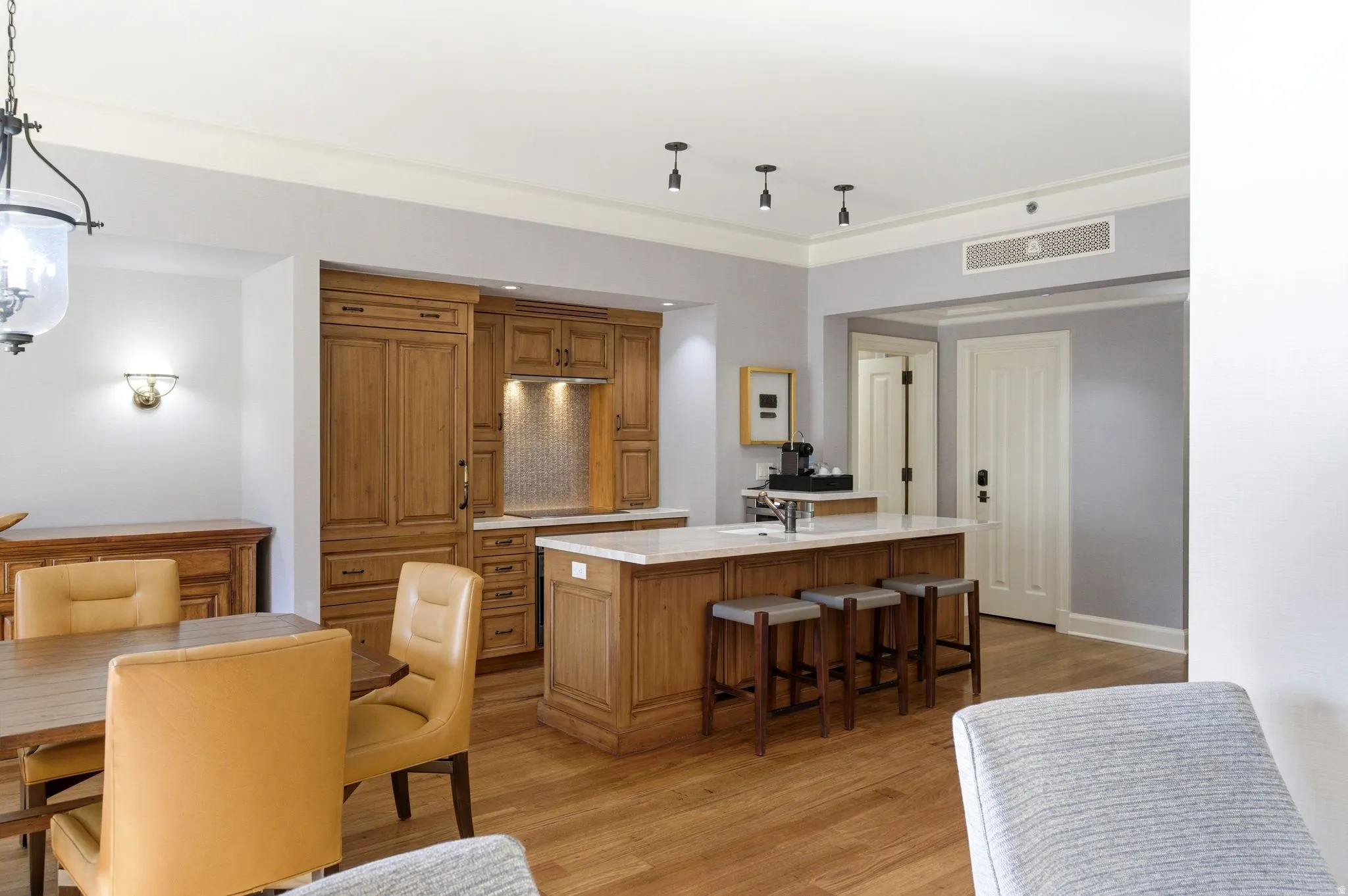Kitchen island with a white countertop and seating for three, flanked by custom wood cabinetry featuring integrated appliances and a tiled backsplash