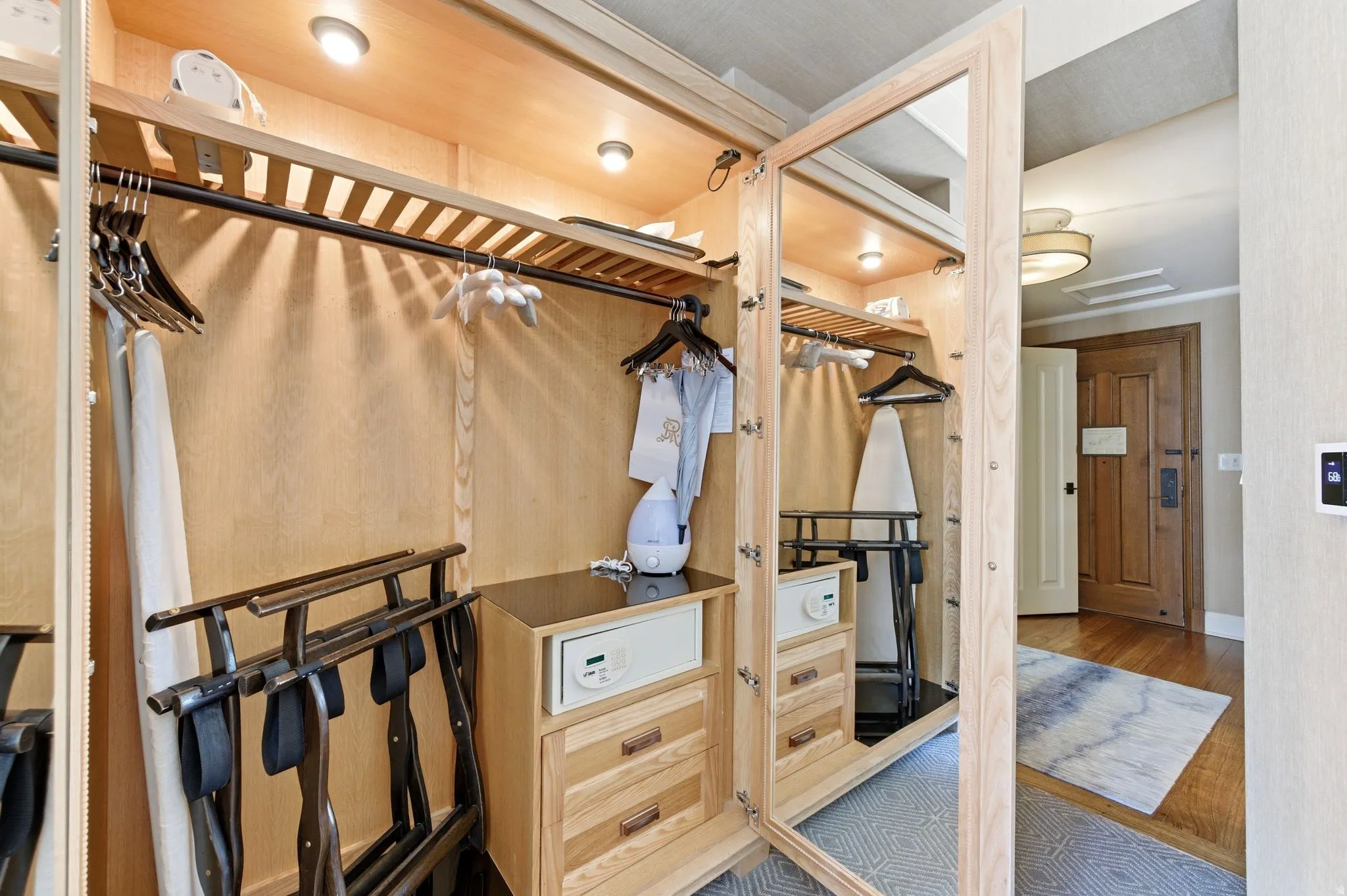 Built-in wood-finish closet system featuring integrated lighting, multiple hanging rods, and wood-finish drawers