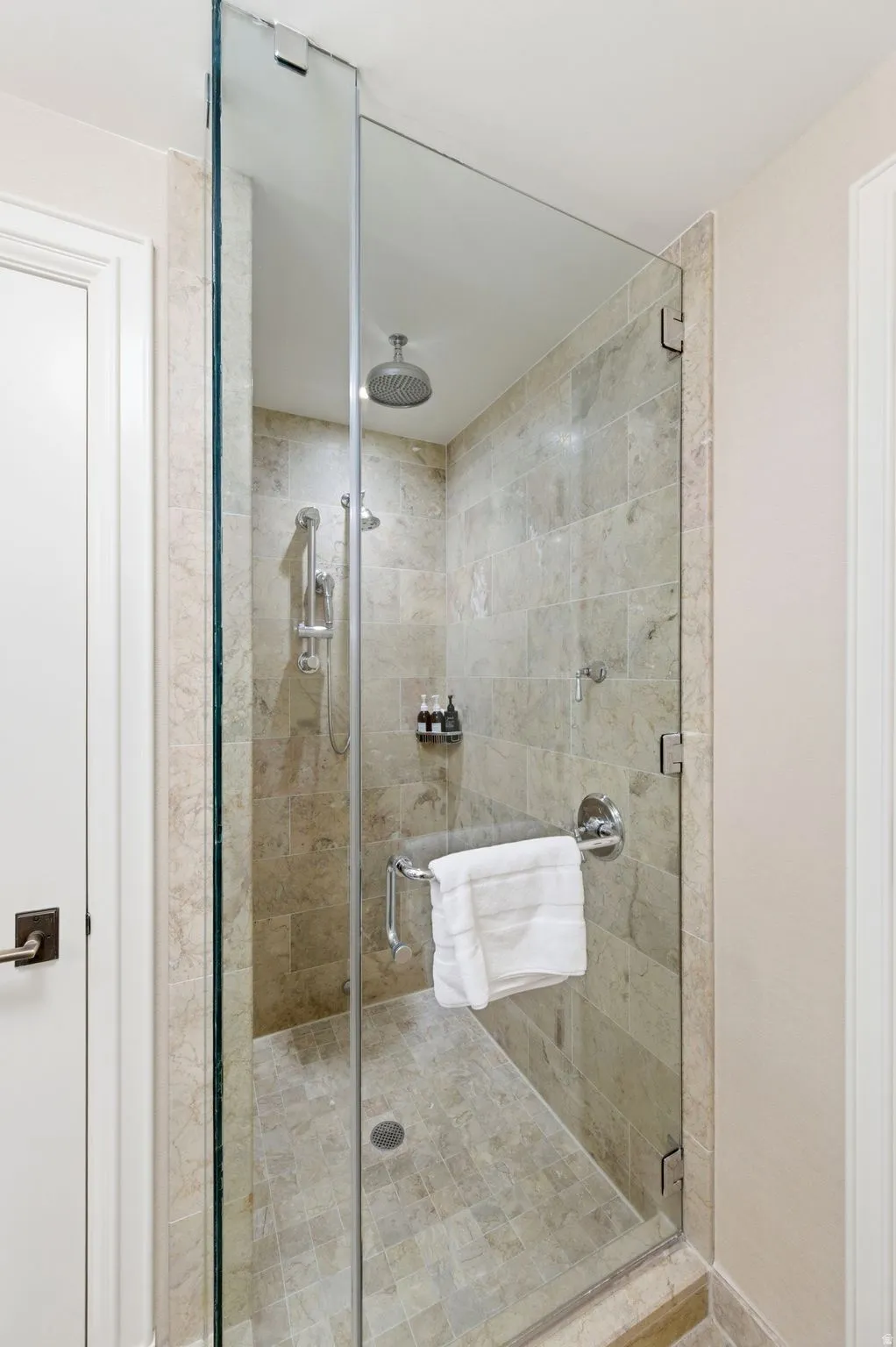 Walk-in shower featuring full-height stone-look tile, rain shower head, handheld shower fixture, and a clear glass enclosure