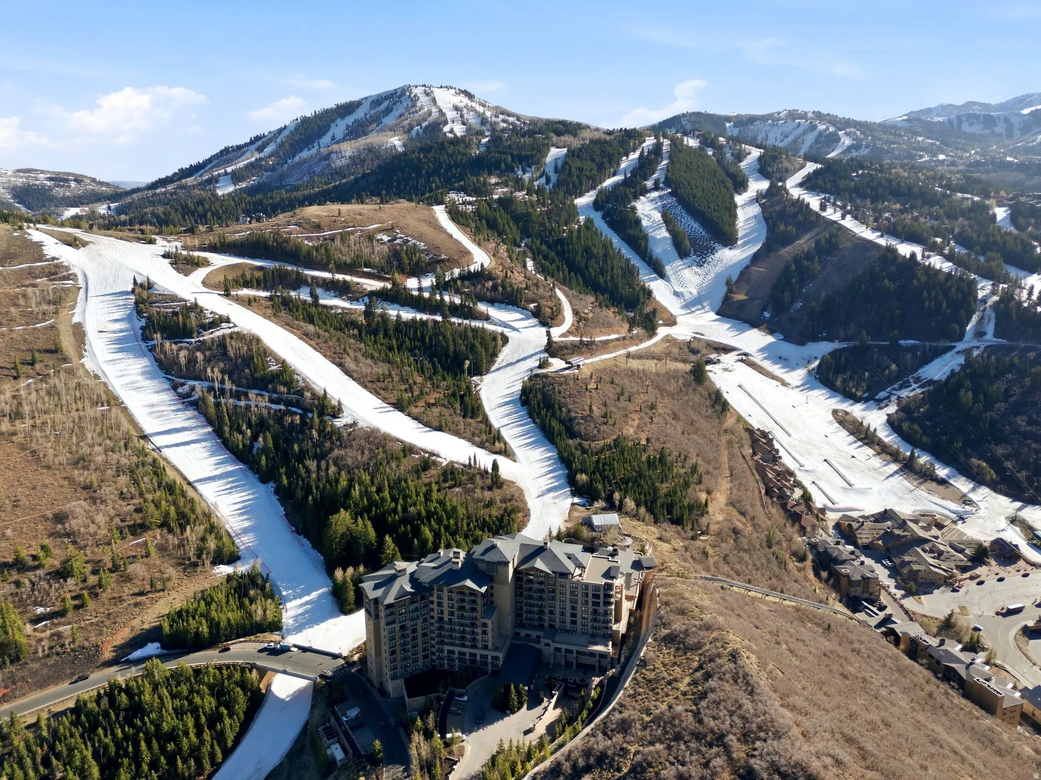 Mountain landscape featuring multiple ski slopes, forested areas, and a large resort building with stone and dark-toned facades