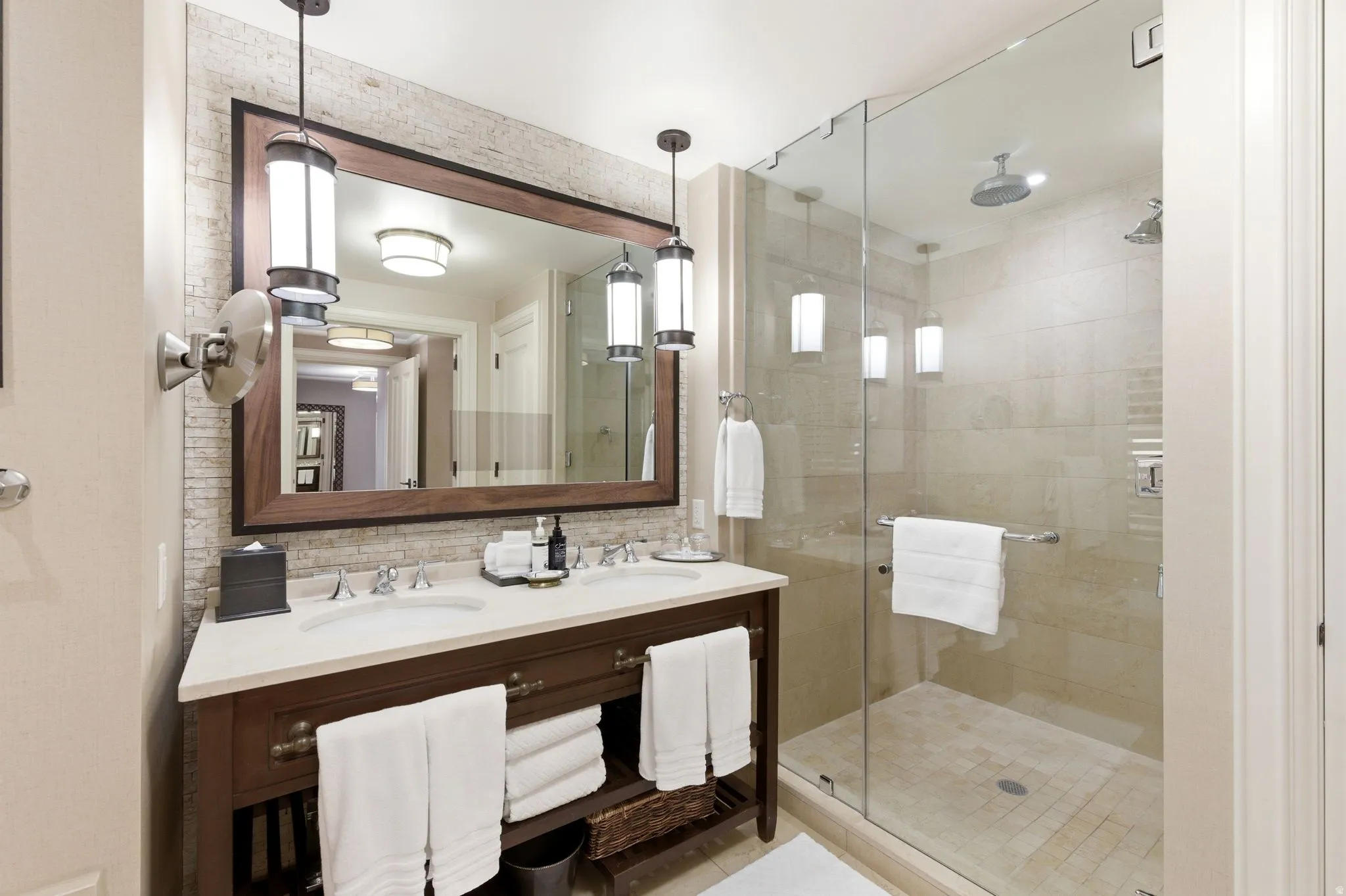 Bathroom featuring a dual vanity with a light-toned countertop, a frameless glass shower enclosure, a rain showerhead, a wall-mounted showerhead, and pendant light fixtures