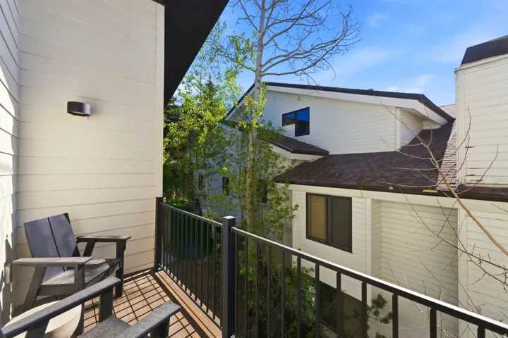 Private balcony featuring wood-finish decking, black metal railing, and a wall-mounted exterior light fixture