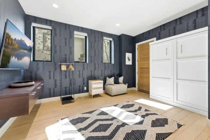 Room featuring light wood-finish flooring, two rectangular windows, a wall-mounted media console, and a built-in white cabinetry unit