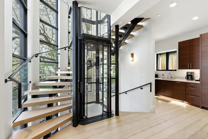 Multi-level living space featuring an integrated elevator, light wood-finish flooring, and a modern floating staircase with glass railing