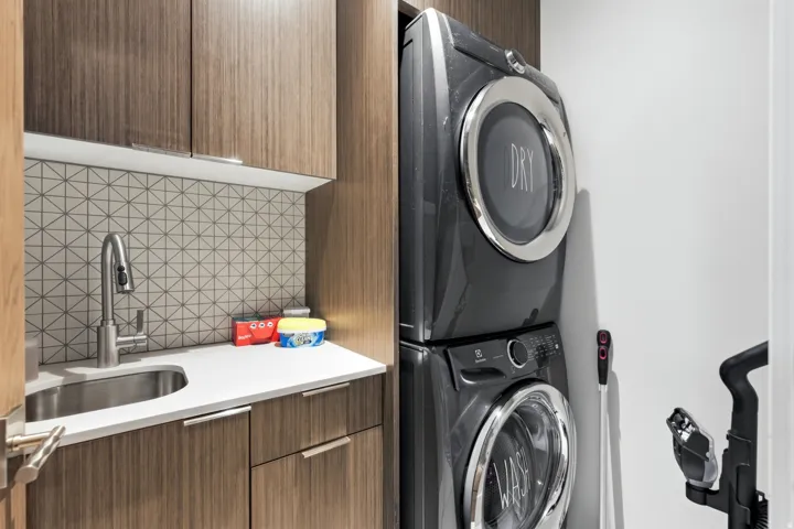 Laundry area featuring stacked appliances, a stainless steel sink, and a geometric-patterned tile backsplash