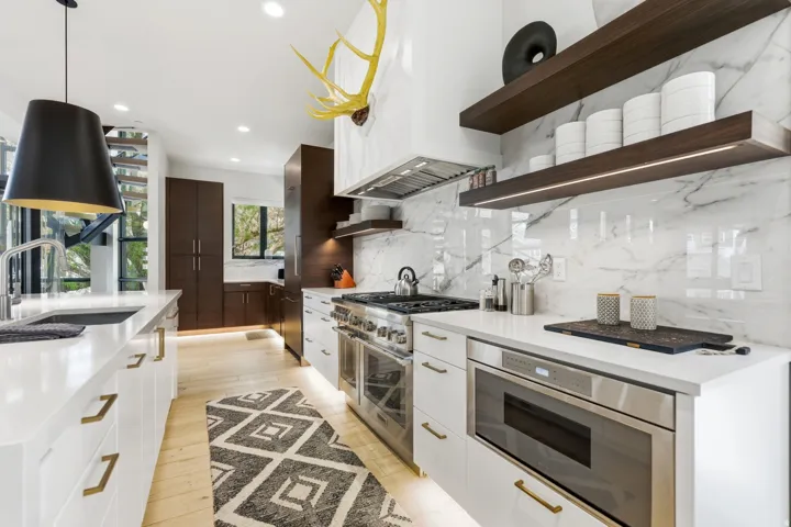Modern kitchen featuring wood-finish flooring, white cabinetry with gold-toned hardware, and a large kitchen island with an undermount sink